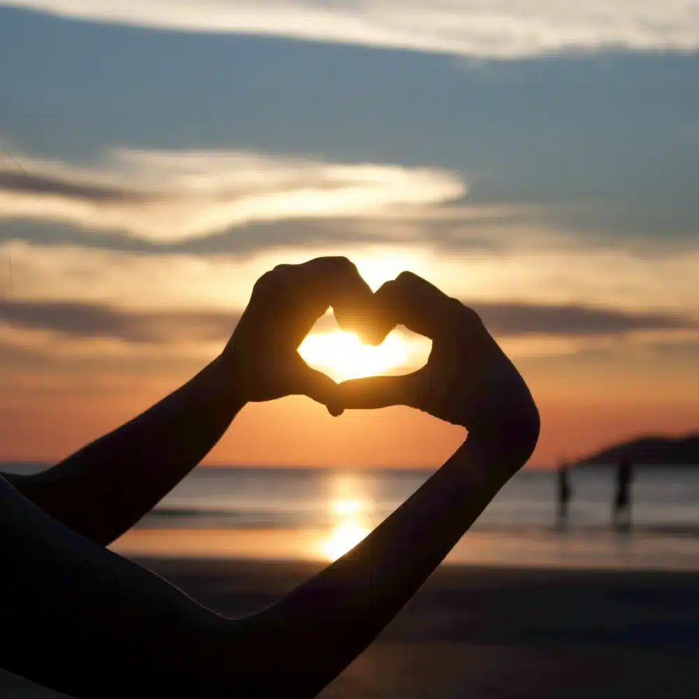 Tirage voyance amour gratuit avec Sophie Vitali Mains formant un cœur devant un coucher de soleil, symbole du blog amour et voyance de Sophie Vitali