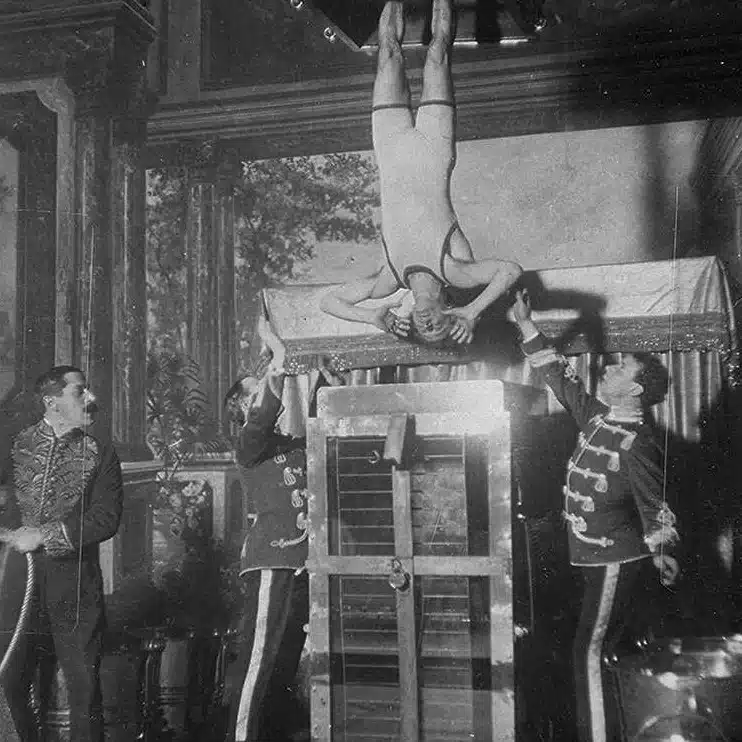 Harry Houdini suspendu la tête en bas, les chevilles bloquées, au-dessus de la cellule de torture chinoise, la cuve d’eau de verre et de métal de son numéro le plus célèbre