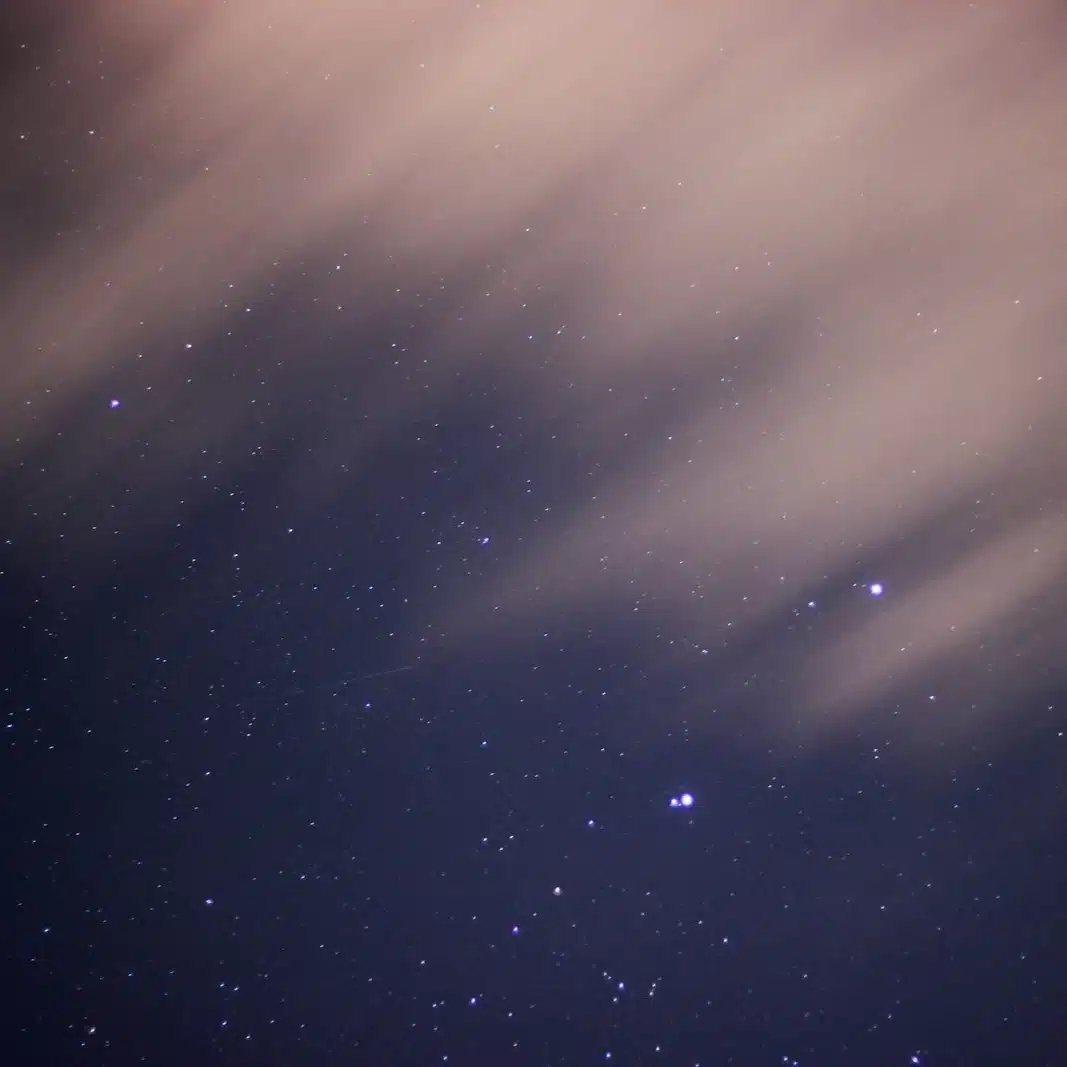 Ciel de nuit étoilé derrière de fins nuages, où un témoin peut apercevoir une lumière qu’il ne sait pas identifier : OVNI, PAN ou UAP